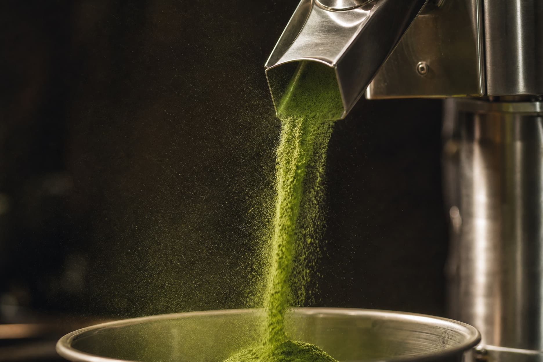 Fine green powder falling from a mill into a steel bowl